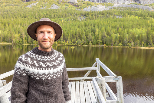 Man enjoying peaceful environment in Norway. Lake and green mountains.
He relaxes on a wooden pier.