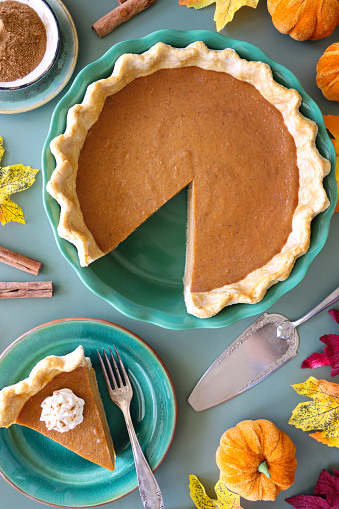 Stock photo showing close-up, elevated view of a tart tin case lined with freeform fluted, pastry that has been filled with a pumpkin puree to make a freshly baked pumpkin pie. Home baking concept.