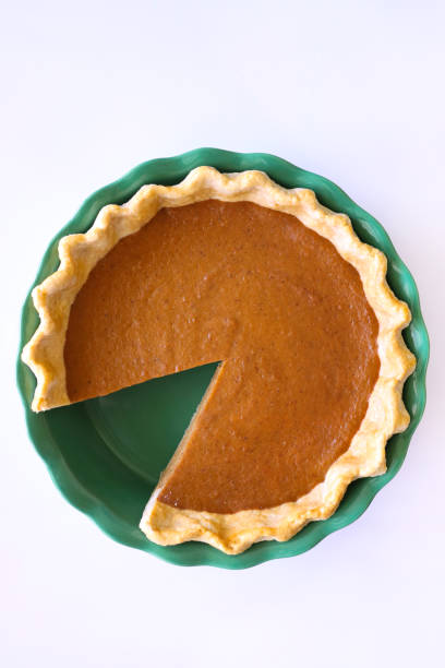 Stock photo showing close-up, elevated view of a tart tin case lined with freeform fluted, pastry that has been filled with a pumpkin puree to make a freshly baked pumpkin pie. Home baking concept.