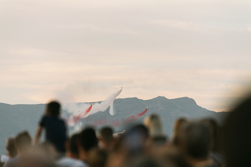 Izmir, Turkey, September, 9, 2023, on Izmir's Liberation Day, the renowned Turkish Stars aircrafts paint the sky with their breathtaking aerial maneuvers. Leaving trails of red and white smoke behind, they capture the awe of the defocused crowd below, who gaze up in admiration and pride