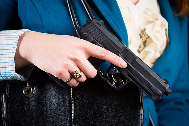 Woman Carrying Handgun A close-up of a woman holding a handgun in a purse. wallet gun stock pictures, royalty-free photos & images