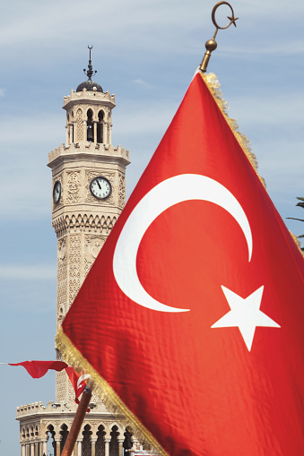 Izmir, Turkey, September 9, 2023: A vibrant photograph showcasing a Turkish flag waving proudly with the renowned Clock Tower of Izmir elegantly standing in the background during the early hours