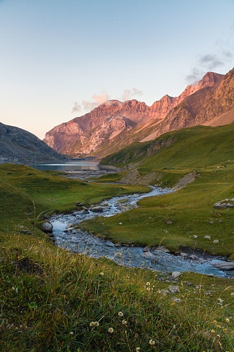 Landscape summer view of the Col du Sanetsch at sunset with a river winding through a green meadow