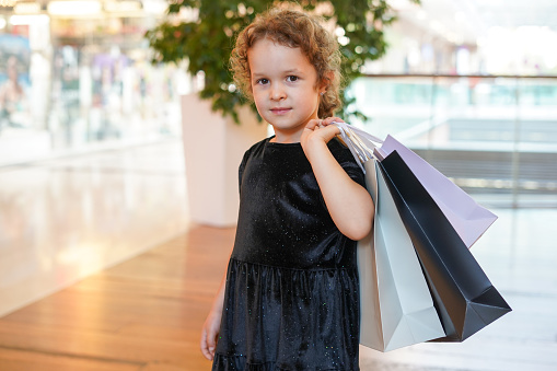 cute child girl in black dress on shopping. portrait of a kid with shopping bags. Black Friday concept