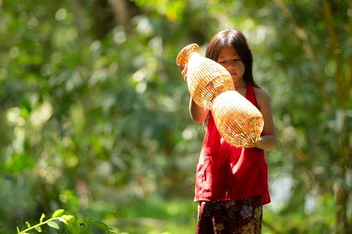 Little asian girl in red dress holding fishing equipment in the forest, Rural Thailand living life concept