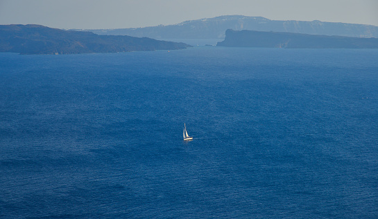A sailing boat going in the middle of the blue and tranquil sea.