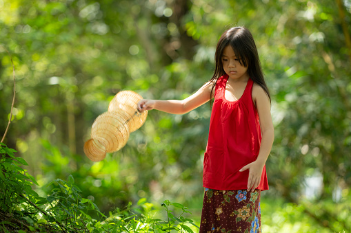 Little asian girl in red dress holding fishing equipment in the forest, Rural Thailand living life concept