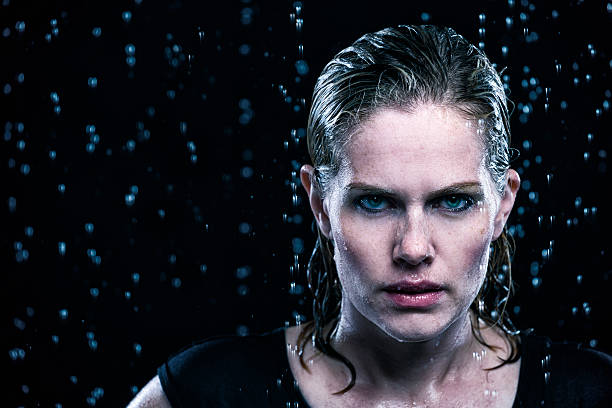 A young woman standing in rain.  Raindrops are blurred all round her and is real water falling.  Photographed in a studio.