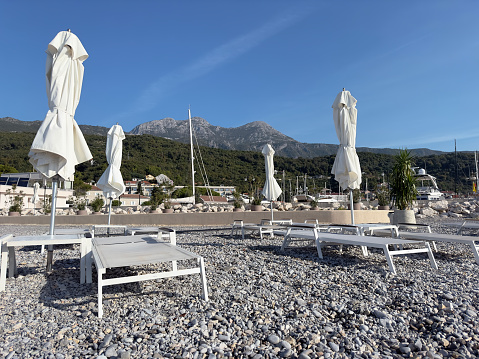 Empty beach showing Sun Loungers and umbrellas on Montenegro beach in shoulder season. Blue sky and mountains in background.