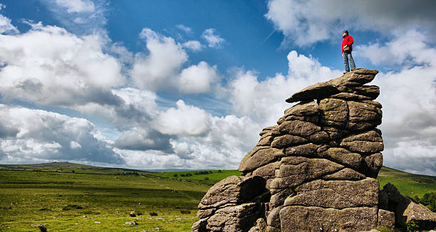 Hiker on top of a Rock A hiker standing on top of a large rock at Hound Tor in Dartmoor England overlooking a valley. outcrop stock pictures, royalty-free photos & images