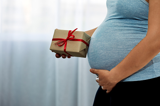 Pregnant Woman holding brown Gift Box in Her Cozy Bedroom with copy space - Anticipating Joyful Motherhood