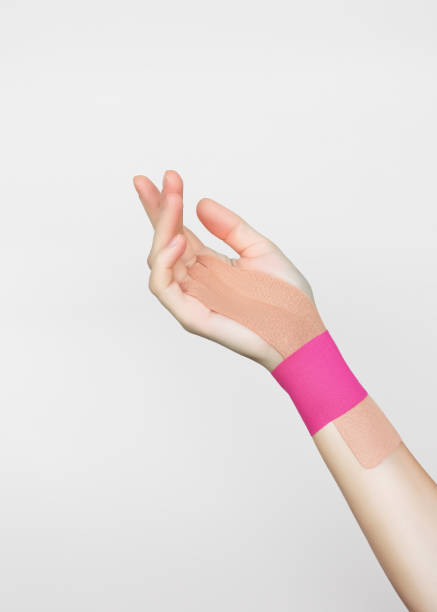 ベージュとピンクのキネシオテープによる女性の手の手首関節の固定 - sprain human joint palm human arm ストックフォトと画像