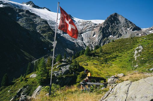 He is sitting below a Swiss flag and glaciated mountains