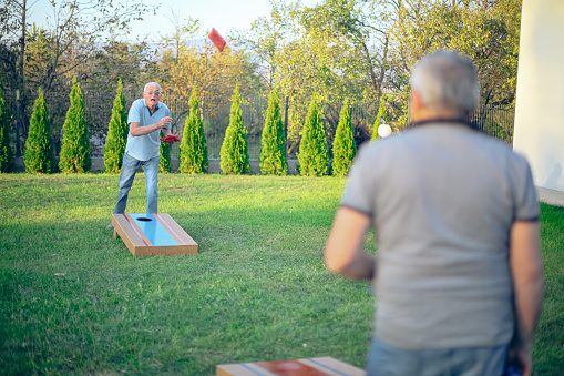 Two active seniors playing corn hole game in backyard