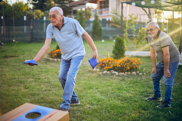 dwóch starych przyjaciół bawi się w kukurydzianą dziurę na podwórku - cornhole leisure games outdoors color image zdjęcia i obrazy z banku zdjęć