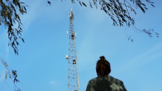 Woman watching on cellular tower station for wireless telecommunication dangerous 3G 4G 5G