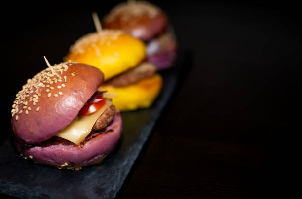 Colored Mini Gourmet Burgers with sesame seeds on black slate board