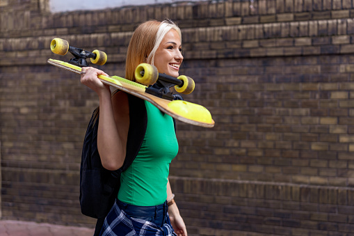 A young woman makes her way through the urban landscape, skateboard in hand, and headphones delivering the soundtrack of her life