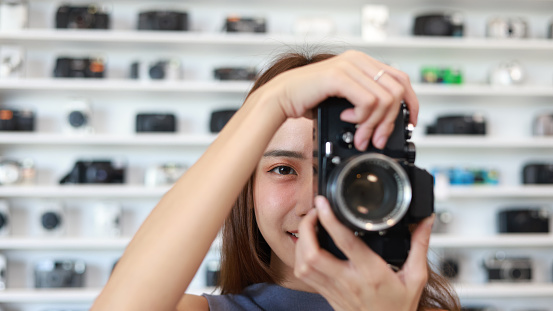 A young Asian woman Taking Photos With an Analog Camera in the camera store .