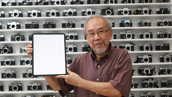 The elder man shows the blank screen of a tablet in the camera store, copy space tablet