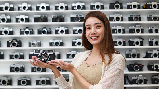A young Asian woman holds an old model camera in her hand at the  Small camera shop.