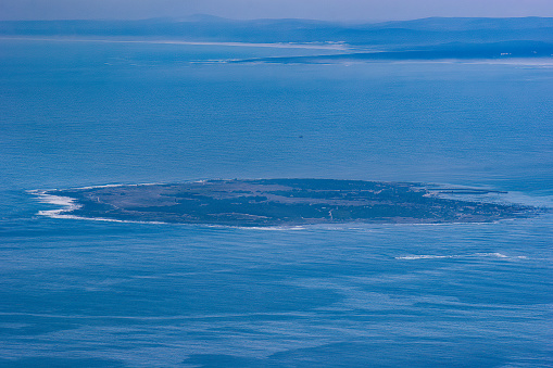 Robben Island off the coast of Cape Town as viewed from Table Mountain in the Cape Province. The Island was a prison from the end of the 17th century, starting with the Dutch. Former South African President, Nelson Mandela spent 18 of the 27 years of imprisonment, in the maximum security prison on the island. Today, it is a popular tourist destination. Photo shot in the afternoon sunlight from atop Table Mountain; horizontal format. Copy space. No people.