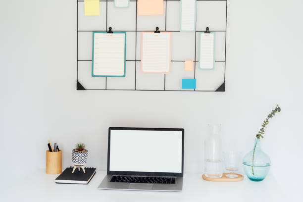istock Modern workplace - white desk with laptop mockup empty screen, grid mood board with pinned notes and check lists for plans, office supplies at work space in home office room interior. 1743121531