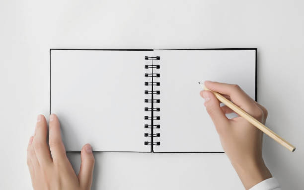 istock woman writes or draws in a square spiral notebook with blank white pages on white background. mockup, space for text. education concept 1743122096