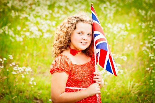 Beautiful 11 year old girl with a British flag standing in a fairy tale field of wildflowers