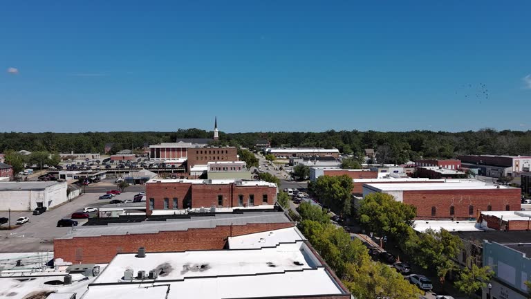 Flock of pigeons flying over Camden Clock Tower. Fly above traffic on Broad Street in Camden, South Carolina. Aerial footage with forward-passing the tower camera motion