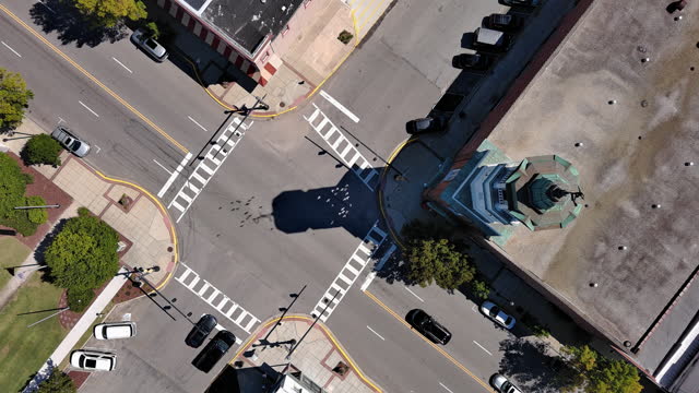 Flock of pigeons flies over the Broad Street intersection with car traffic in Camden, SC at noon. Clock Tower spire rise above the street. Top view. Aerial footage with static camera motion