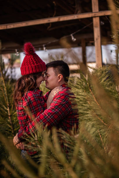 abraços carinhosos de jovem casal apaixonado entre mercado verde de árvores de natal na cidade. - christmas tree standing clothing adventure - fotografias e filmes do acervo