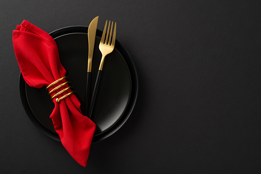 Black Friday grandeur: top view high-class table setting featuring fine dining essentials, dishes, cutlery, red napkin in gold ring on stylish black backdrop. Ideal for advertising your special deals