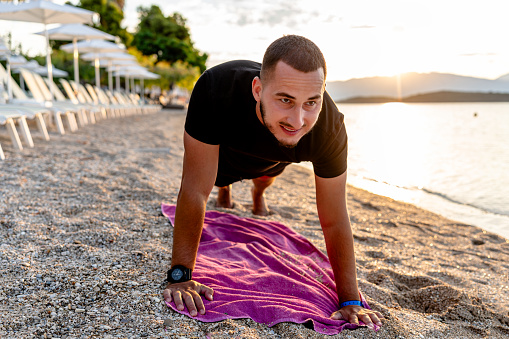 The young man, with determination in his eyes, powers through a series of push-ups, using the beach's natural setting to enhance his workout