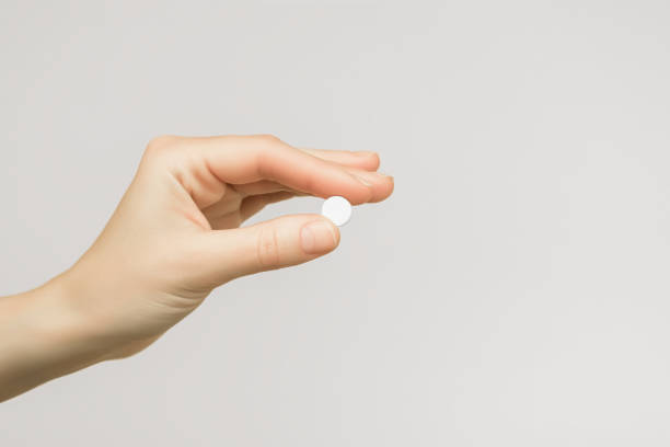 istock female hand holding a round white pill on a grey background 1743199279
