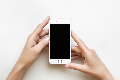 female hands hold iPhone with blank black screen on white table background