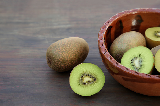 Whole and cut fresh kiwis on wooden table, closeup. Space for text