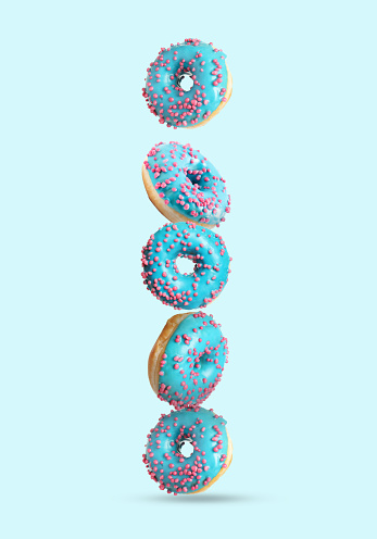 Tasty donuts with sprinkles falling on light blue background