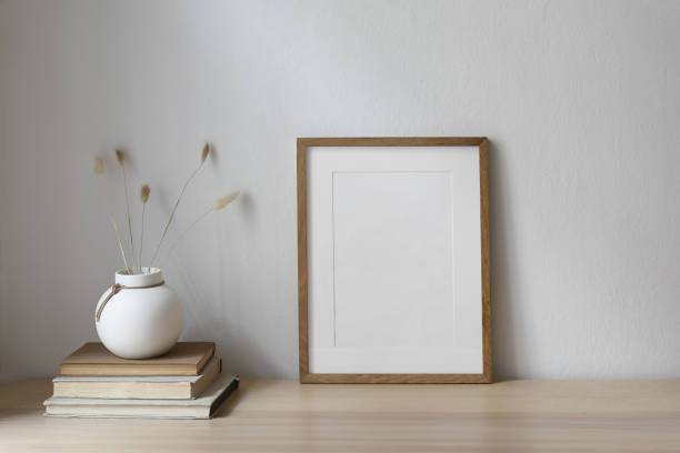 istock Vertical blank wooden picture frame mockup on table. Modern round ceramic vase with dry bunny tails, Lagurus ovatus grass and old books. White wall background. Scandinavian interior, home office. 1743263263