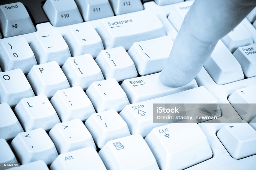 Enter Key A man's finger pressing the "Enter" key on a typical computer keyboard. Blue tone. Computer Stock Photo