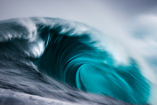 Artistically captured blue curved wave breaking in the open ocean over a shallow reef bombora. Photographed off the south west coast of Australia.