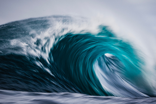 Artistically captured blue curved wave breaking in the open ocean over a shallow reef bombora. Photographed off the south west coast of Australia.