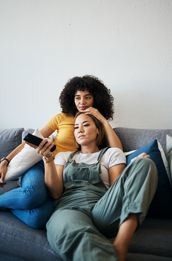 Love, television and a lesbian couple watching a movie on a sofa in the living room of their home together. Relax, LGBT and a woman with her girlfriend enjoying series on a streaming service