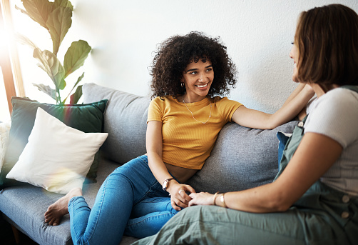 Discussion, love and lesbian couple relaxing on a sofa in the living room talking and bonding. Happy, conversation and young interracial lgbtq women speaking and resting together in lounge at home.