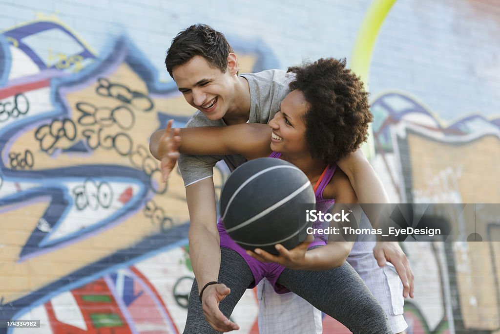 Woman Playing a Game of Basketball Against Man Group of friends playing a game of one on one Basketball in a Berlin's city park. Young woman is fighting for control of the ball, young man is trying to knock ball from her hands.  Horizontal shot.  20-24 Years Stock Photo