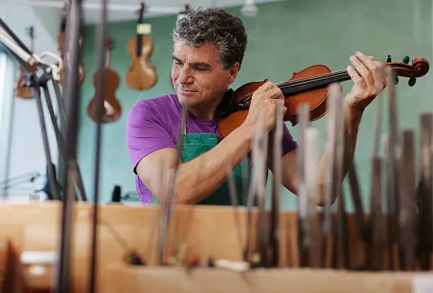 Violin maker testing a violin in his workshop. Horizontal shot.http://www.zweig-industries.de/bilder/lightbox-istock/hhp3violin.jpg
