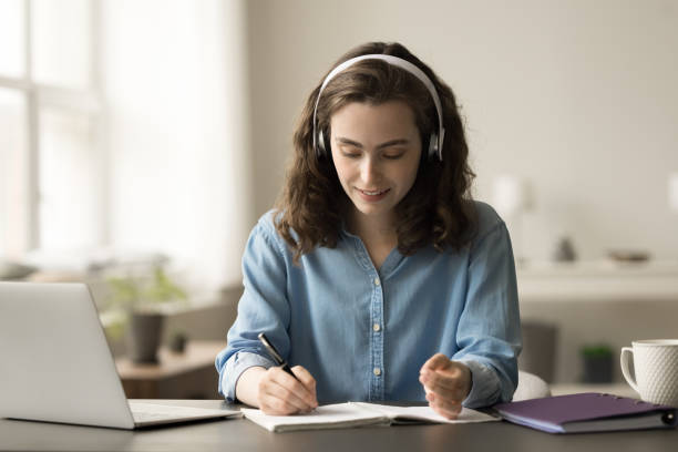 istock Positive hardworking online student girl in headphones writing summary notes 1743368823