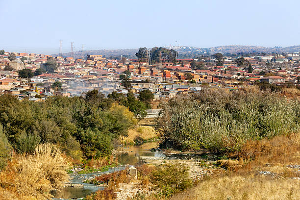 Alexandra township and Jukskei river The Jukskei river going through the township of Alexandra (Alex) was established in 1912 and is close to the center of Johannesburg. It covers an area of over 800 ha (including east bank) and its infrastructure was designed for a population of about 70,000. Current population estimates vary widely and have been put at figures ranging from 180,000 to 750,000. Its original stands of size of 500-600 sq.m are characterized by sizeable houses of reasonable stock but usually with 3 – 6 additional separate rooms built in the original gardens, each usually housing an additional family who rent from the main householder. The additional rental units, which provide a significant income to the main householder, are termed “backyard shacks” although many are of brick or block construction of reasonable quality. There are an estimated 20,000 shacks of which approximately 7,000 are located in “backyards” alexandra township photos stock pictures, royalty-free photos & images