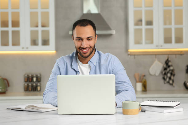istock Young man working on laptop at desk in kitchen. Home office 1743426740