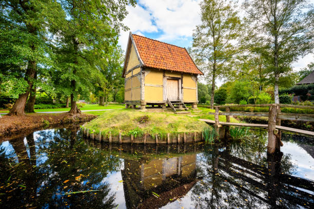 Historical shed in typical style with half-timbered structure and clay surrounded by a moat and idyllic greenery, blooming flowers and wooden bridge in the public spa park of Bad Zwischenahn (Germany)